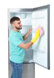 Photo of Young man cleaning refrigerator with rag on white background