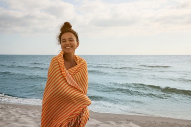 Beautiful African American woman with beach towel on seashore