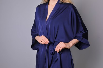 Photo of Woman in beautiful dark blue silk robe on grey background, closeup