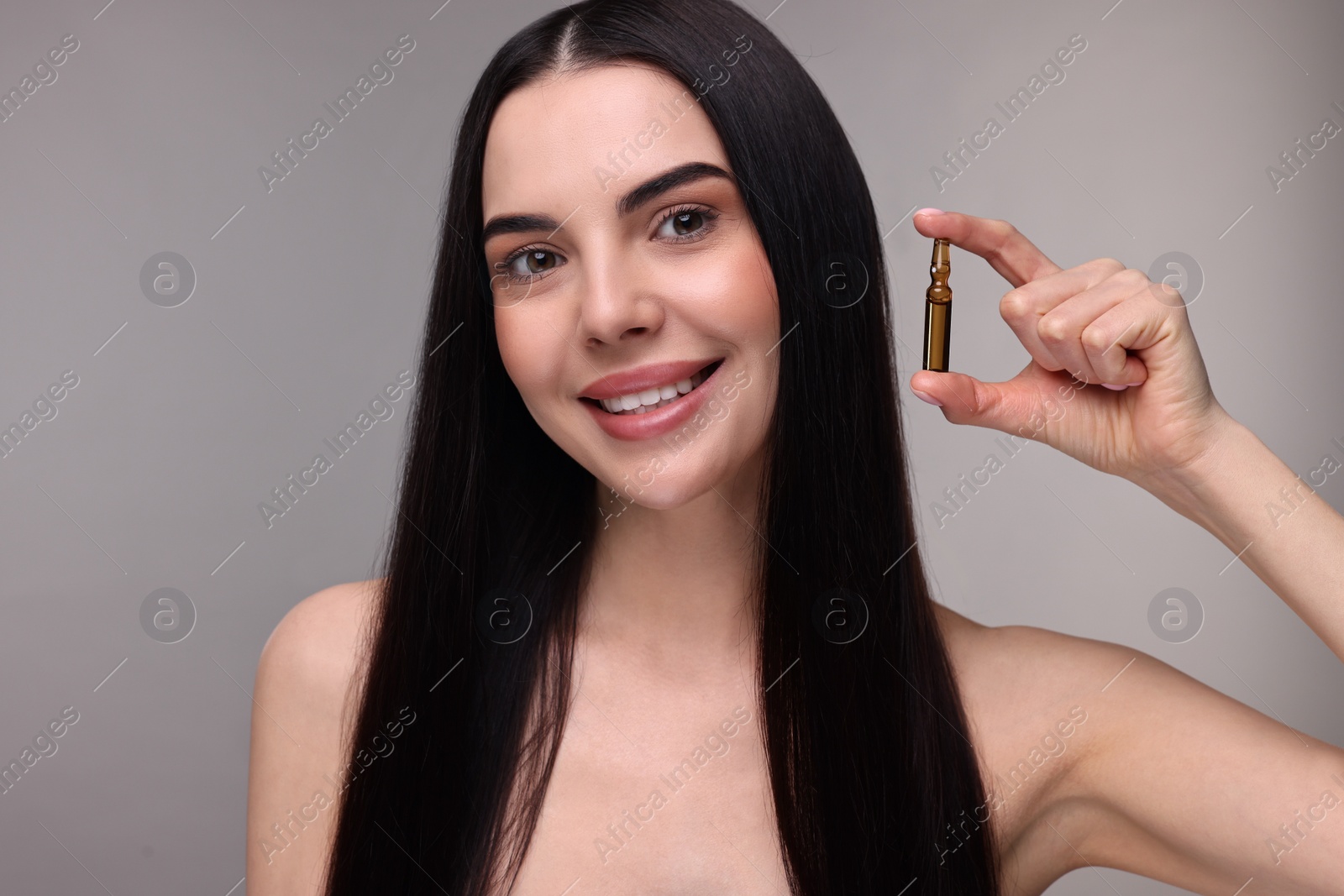 Photo of Beautiful young woman holding skincare ampoule on grey background