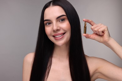 Beautiful young woman holding skincare ampoule on grey background