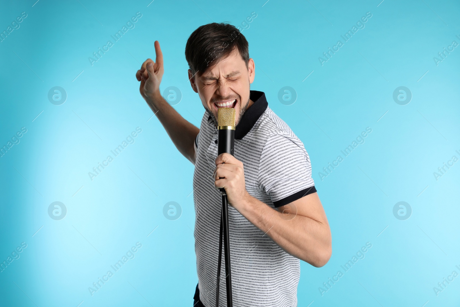 Photo of Handsome man in casual clothes singing with microphone on color background