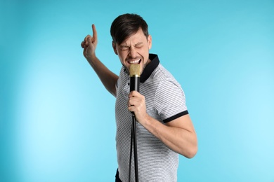 Photo of Handsome man in casual clothes singing with microphone on color background