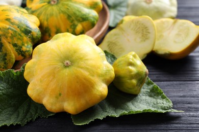 Photo of Fresh ripe yellow pattypan squashes with leaves on black wooden table, closeup