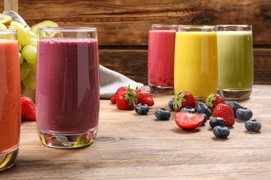 Photo of Glasses with different tasty smoothies and ingredients on wooden table