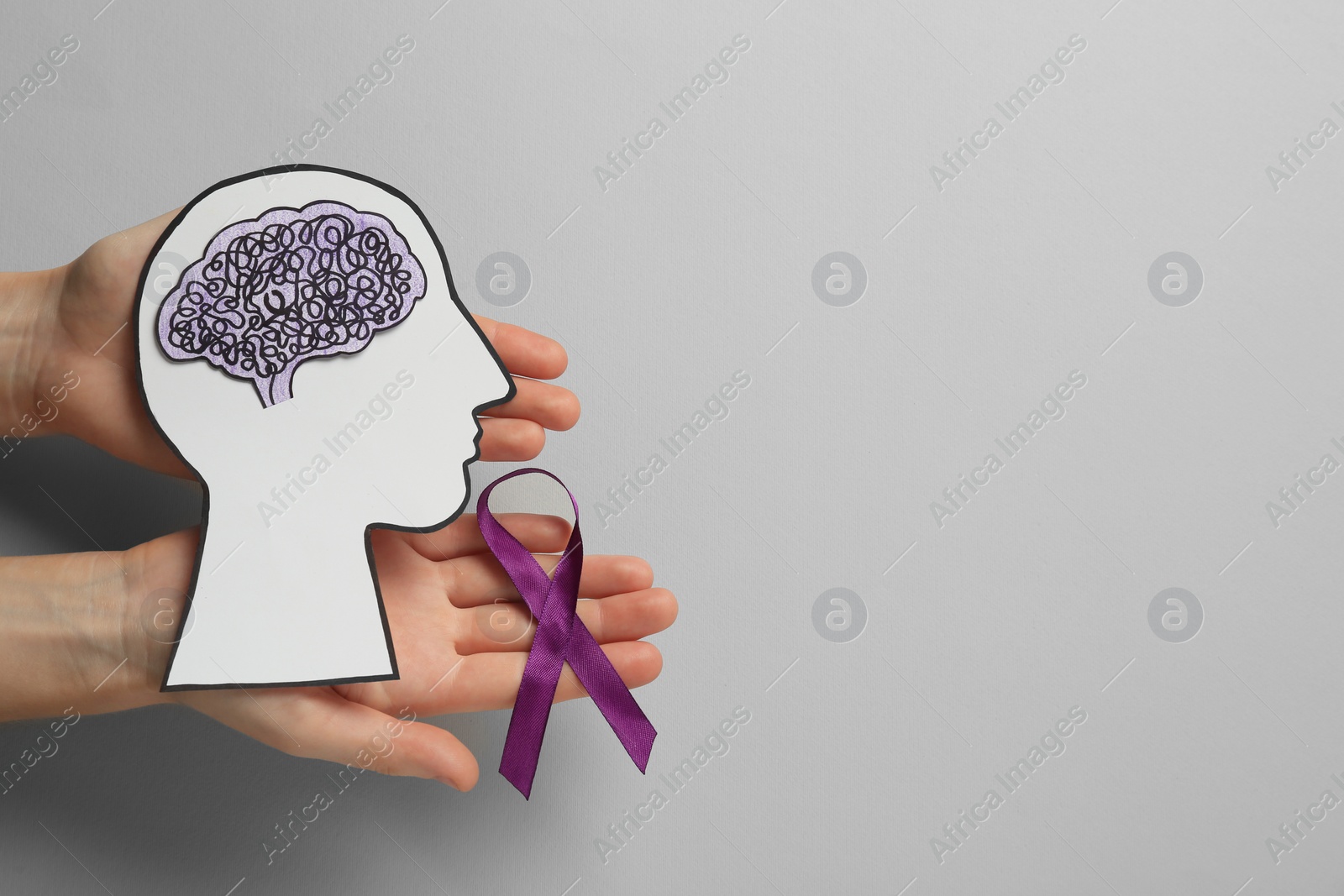Photo of Top view of woman holding human head cutout with brain and purple ribbon on light grey background, space for text. Epilepsy awareness