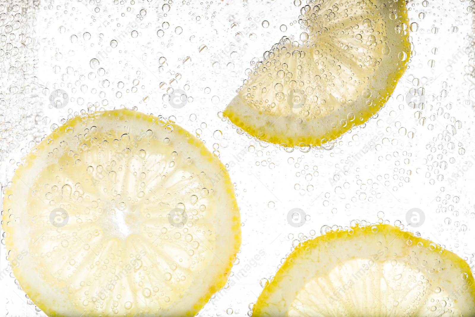 Photo of Juicy lemon slices in soda water against white background, closeup