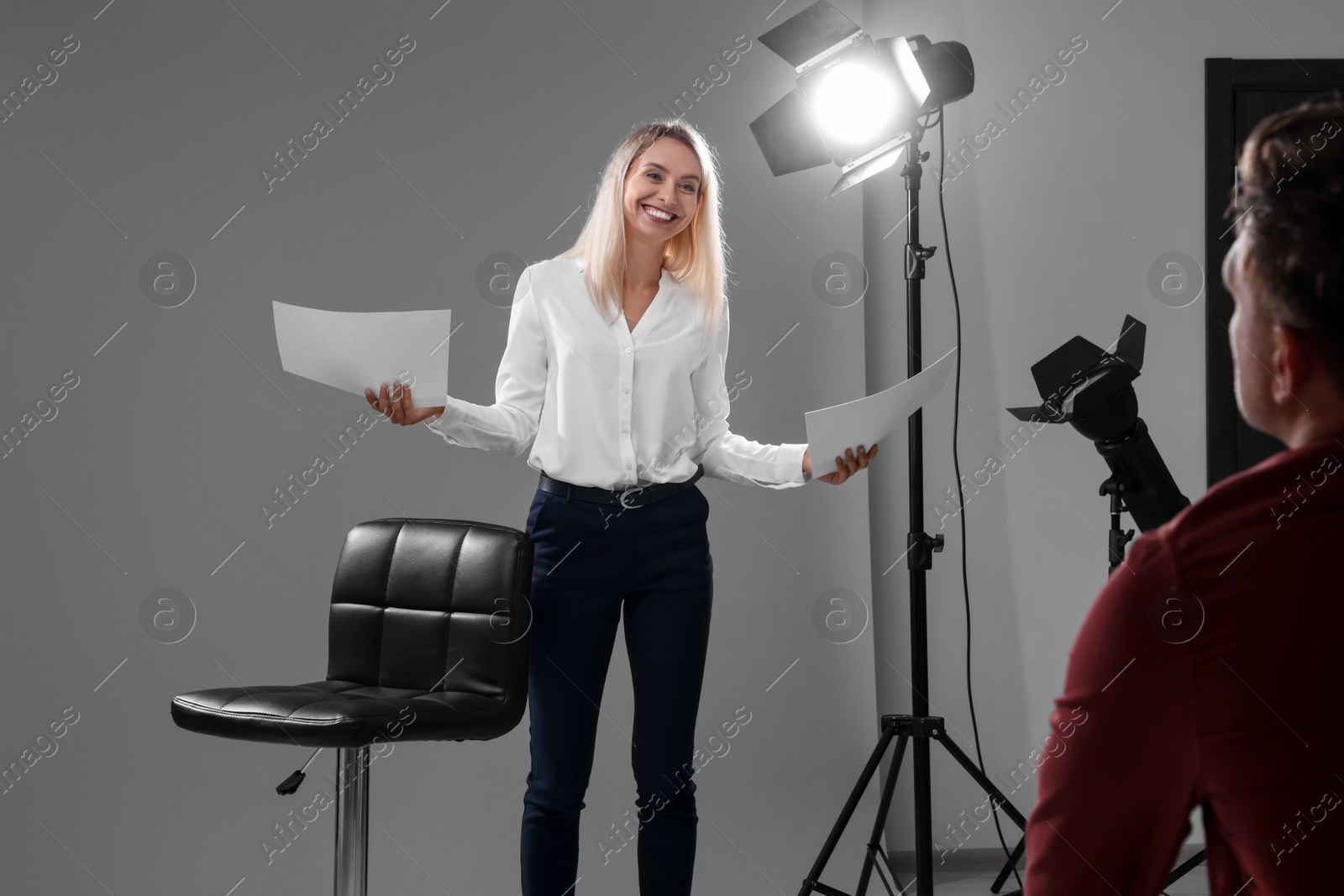 Photo of Emotional woman with script performing in front of casting director against grey background in studio