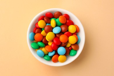 Photo of Bowl with tasty colorful candies on beige background, top view