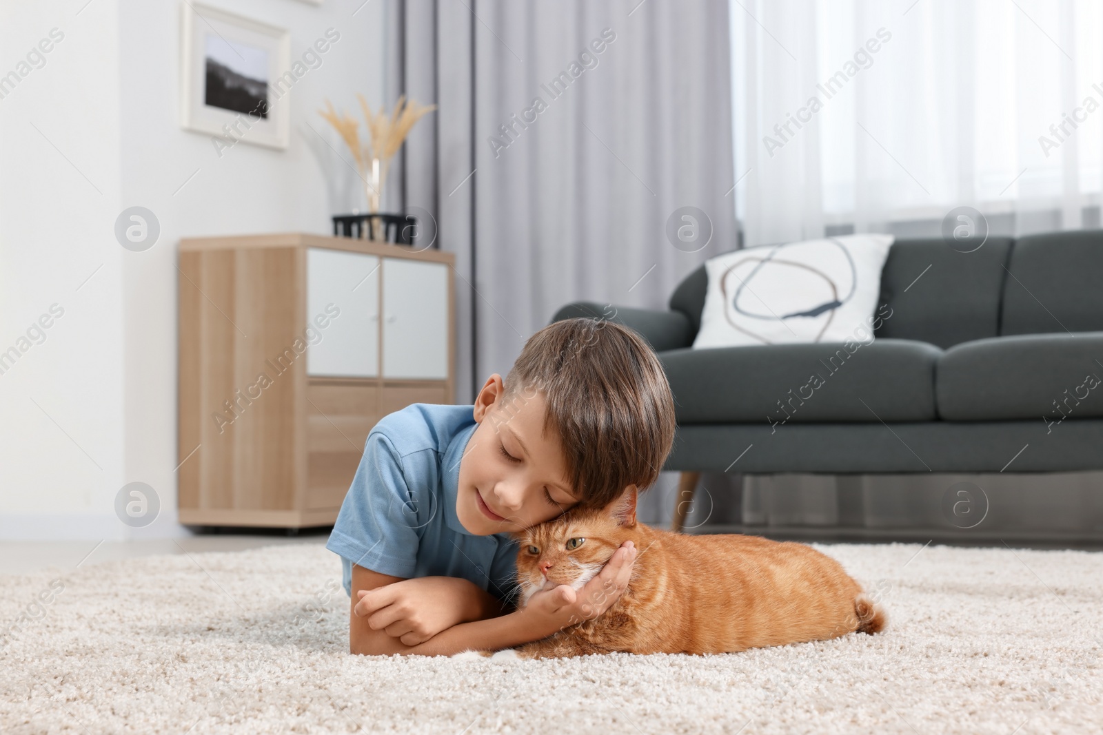 Photo of Little boy with cute ginger cat on soft carpet at home