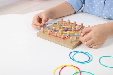 Photo of Motor skills development. Girl playing with geoboard and rubber bands at white table, closeup. Space for text