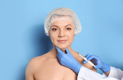 Photo of Mature woman with double chin receiving injection on blue background