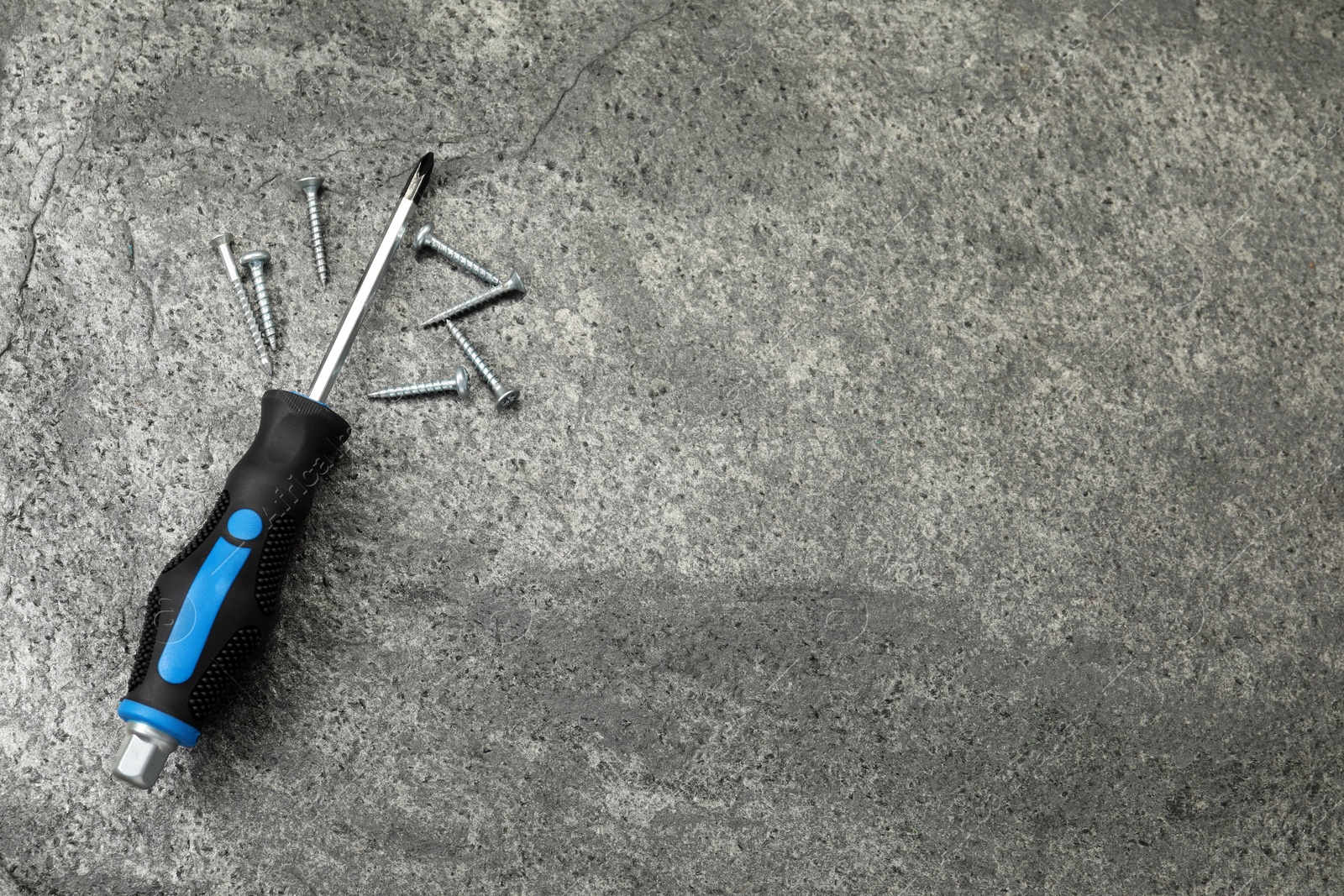 Photo of Screwdriver with black handle and screws on grey table, flat lay. Space for text