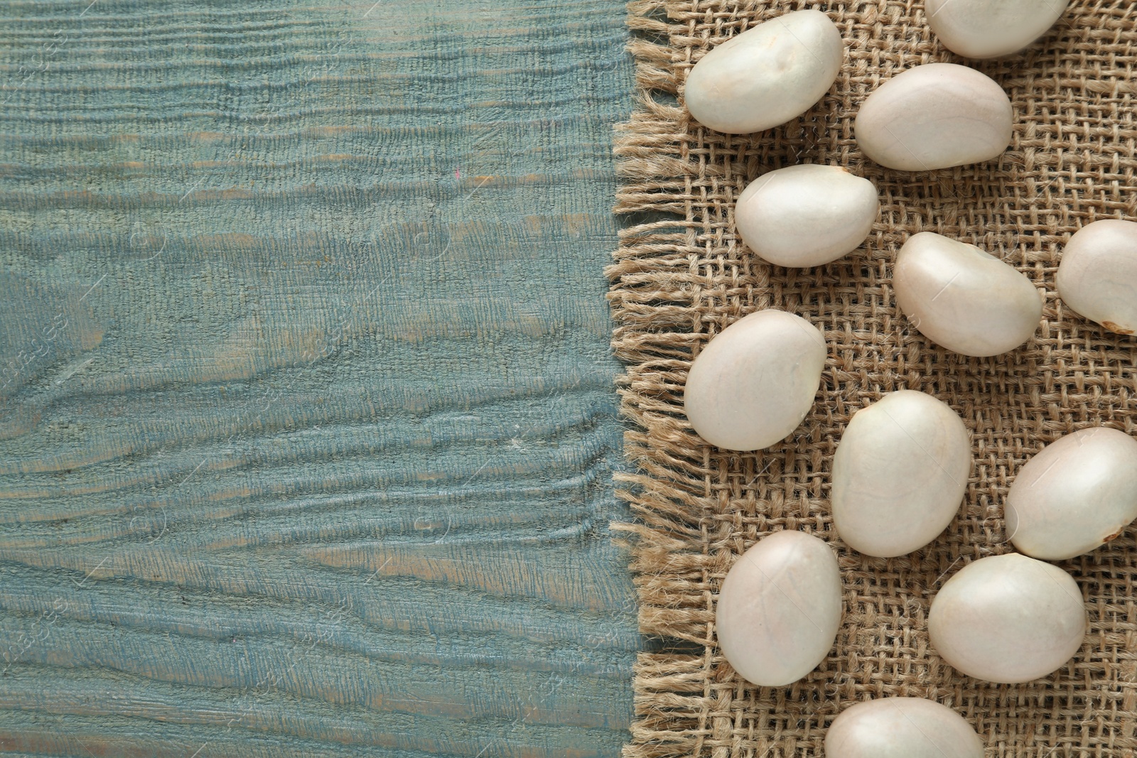 Photo of Raw jackfruit seeds and sackcloth on light blue wooden table, flat lay. Space for text