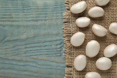 Raw jackfruit seeds and sackcloth on light blue wooden table, flat lay. Space for text