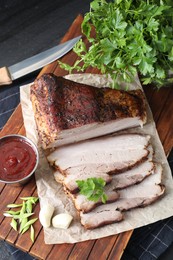 Photo of Pieces of baked pork belly served with sauce and parsley on black textured table, above view