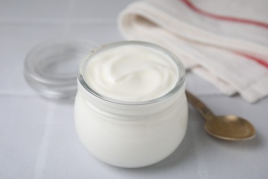 Photo of Delicious natural yogurt in glass jar and spoon on white table, closeup