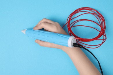 Photo of Boy drawing with stylish 3D pen on light blue background, top view