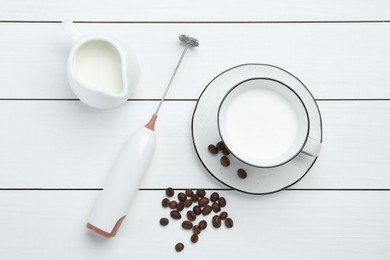 Photo of Flat lay composition with mini mixer (milk frother), whipped milk and coffee beans on white wooden table