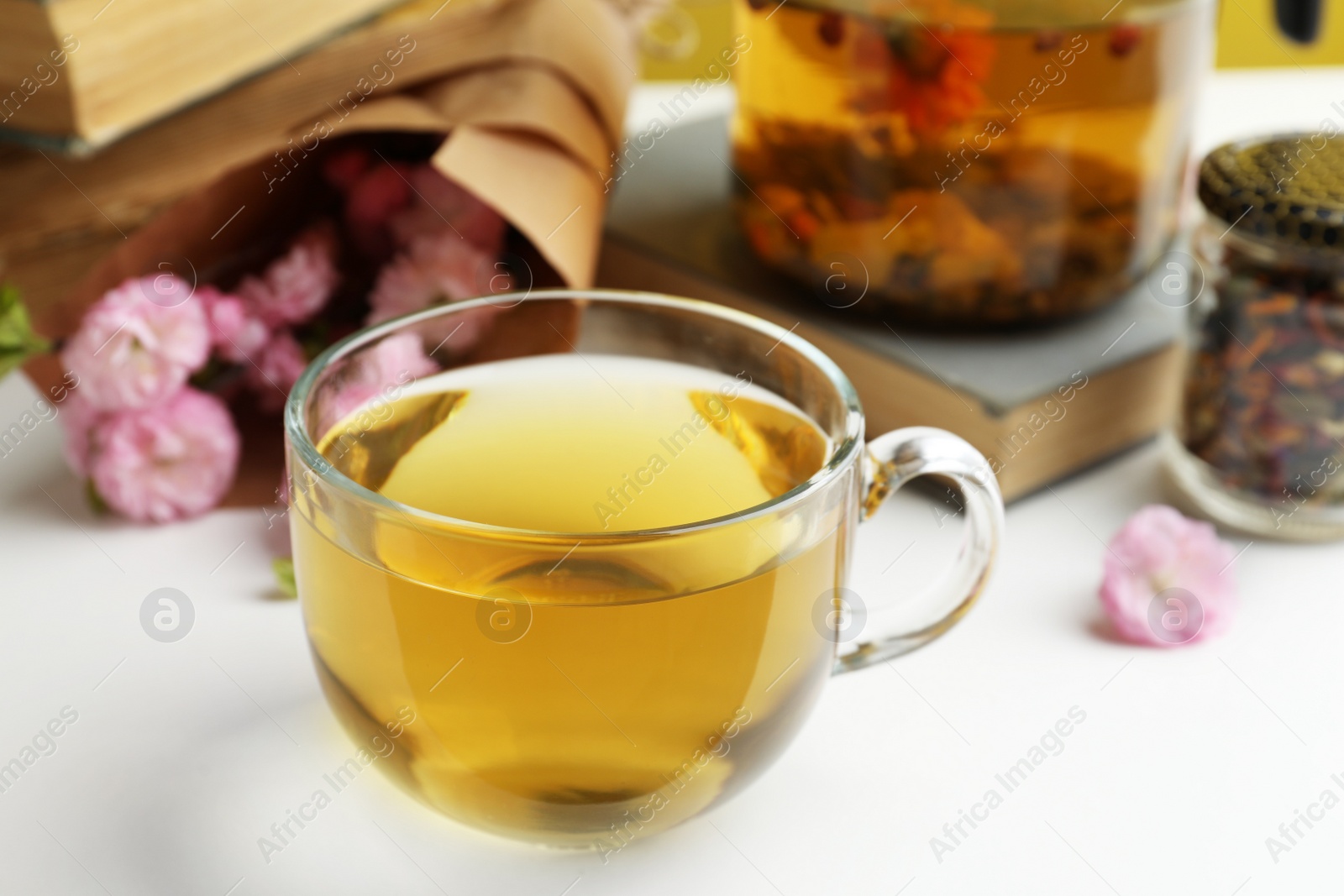 Photo of Glass cup of freshly brewed tea and flowers on light table