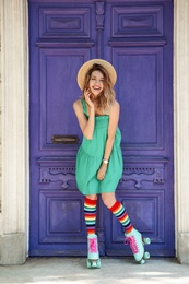 Happy girl with retro roller skates standing near violet door