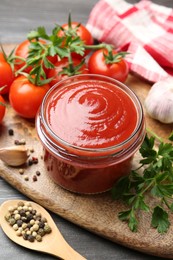 Photo of Tasty ketchup, fresh tomatoes, parsley and spices on grey wooden table