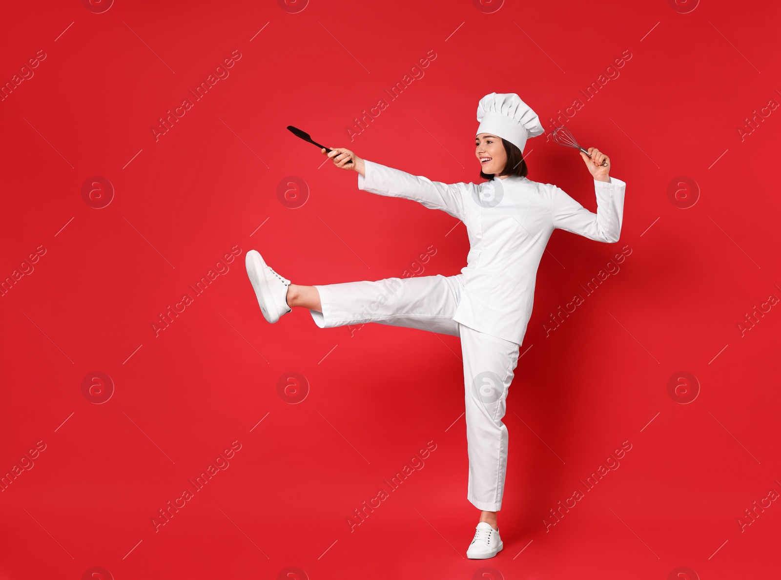 Photo of Happy confectioner holding whisk and spatula on red background