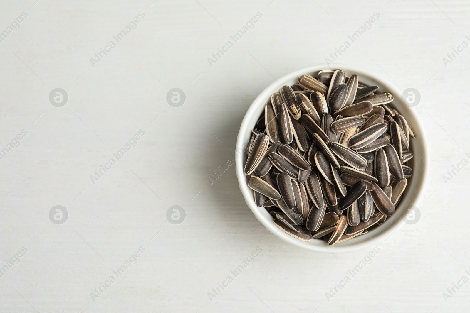 Photo of Organic sunflower seeds on white wooden table, top view. Space for text