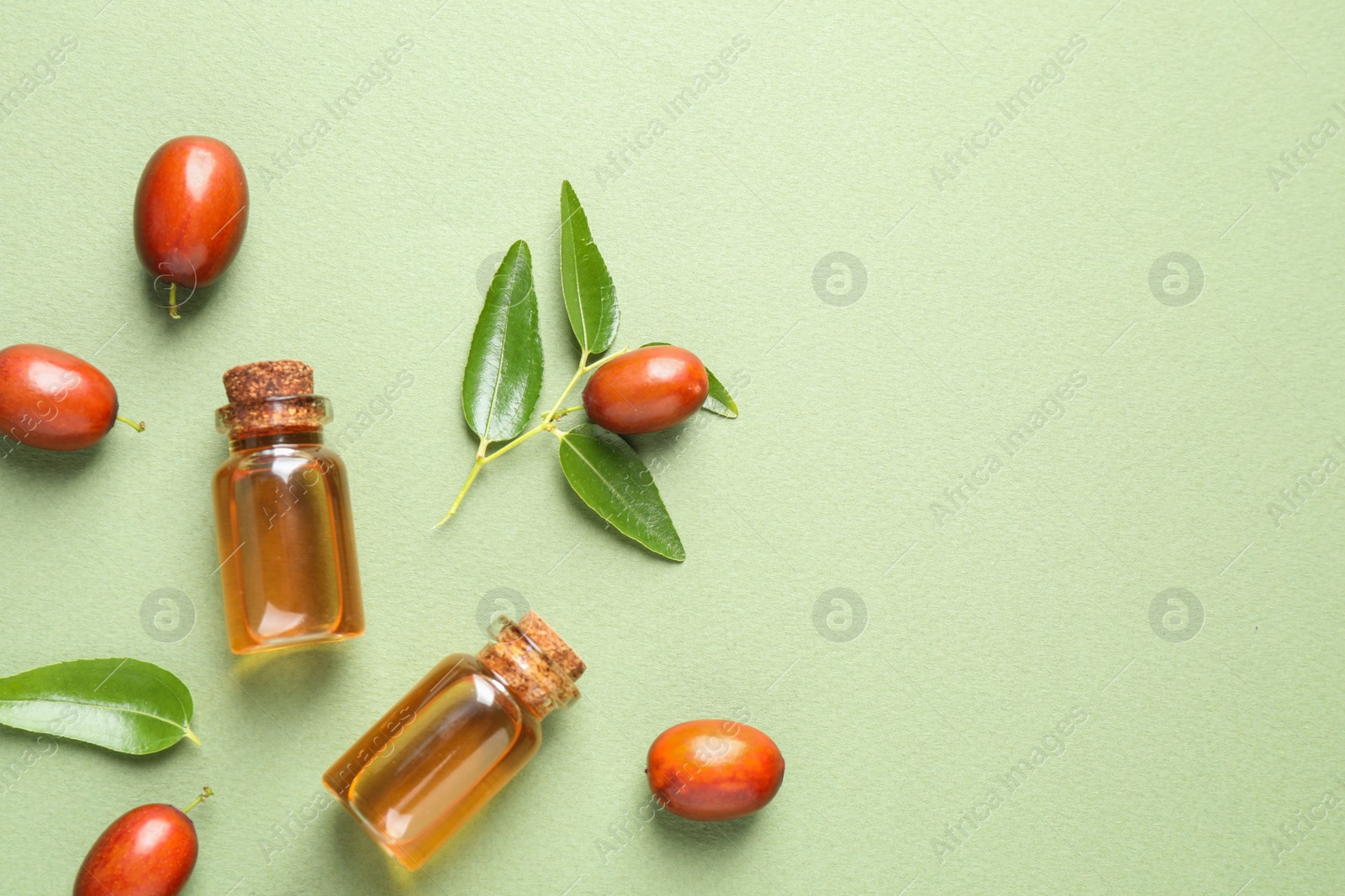 Photo of Glass bottles with jojoba oil and seeds on green background, flat lay. Space for text