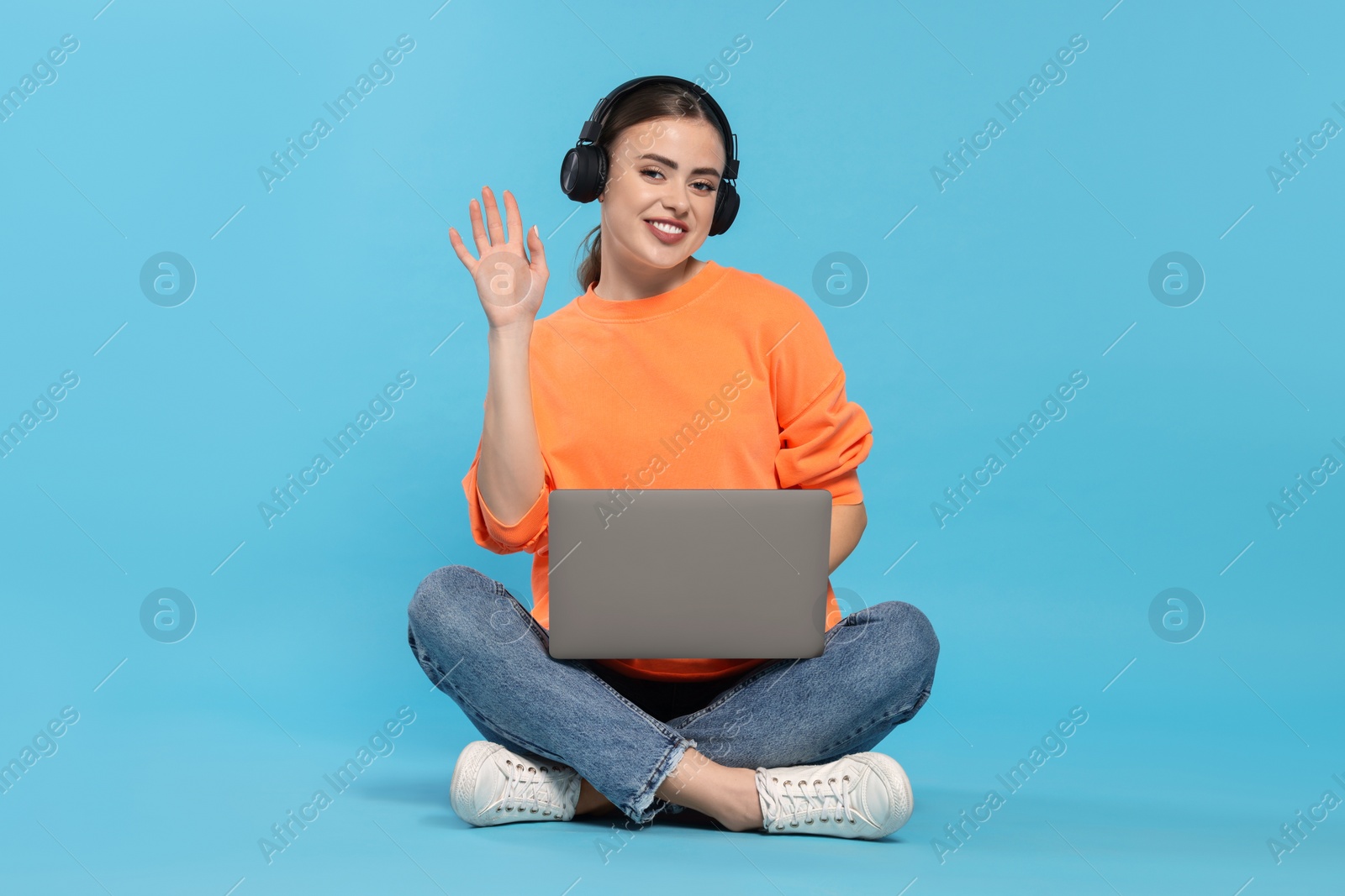 Photo of Happy woman with laptop listening to music in headphones on light blue background