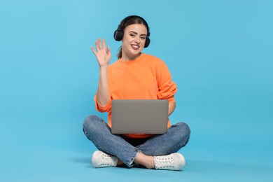 Happy woman with laptop listening to music in headphones on light blue background