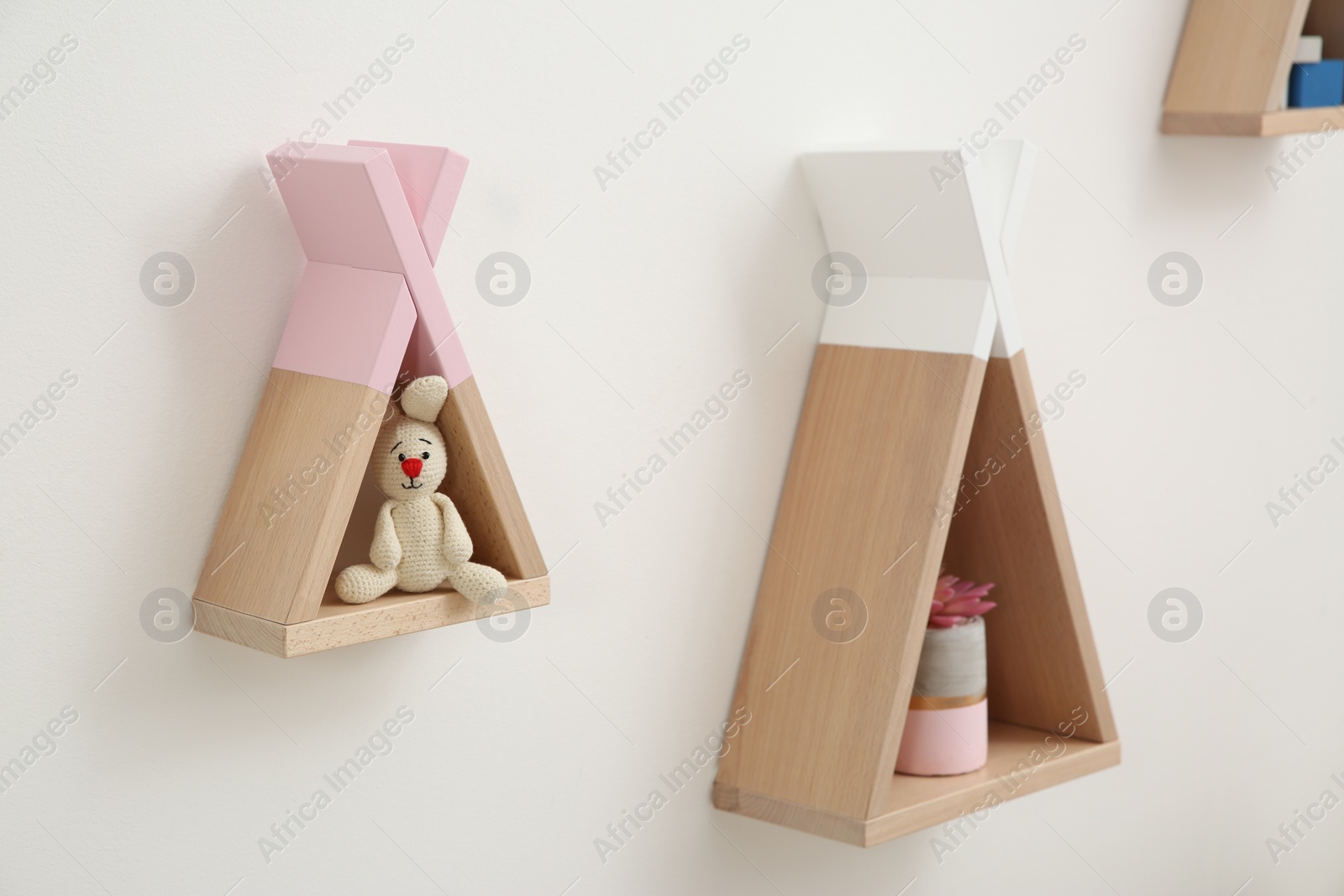 Photo of Funny wigwam shaped shelves with toys on white wall. Baby room interior design