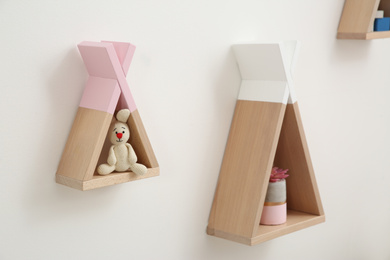 Photo of Funny wigwam shaped shelves with toys on white wall. Baby room interior design