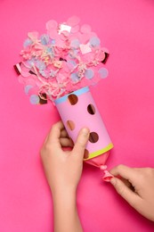 Photo of Woman holding party popper with serpentine and confetti on pink background, top view