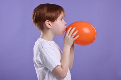 Photo of Boy inflating orange balloon on violet background