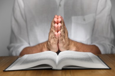 Man with Bible praying at wooden table, closeup