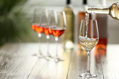 Photo of Pouring white wine from bottle into glass on wooden table, space for text