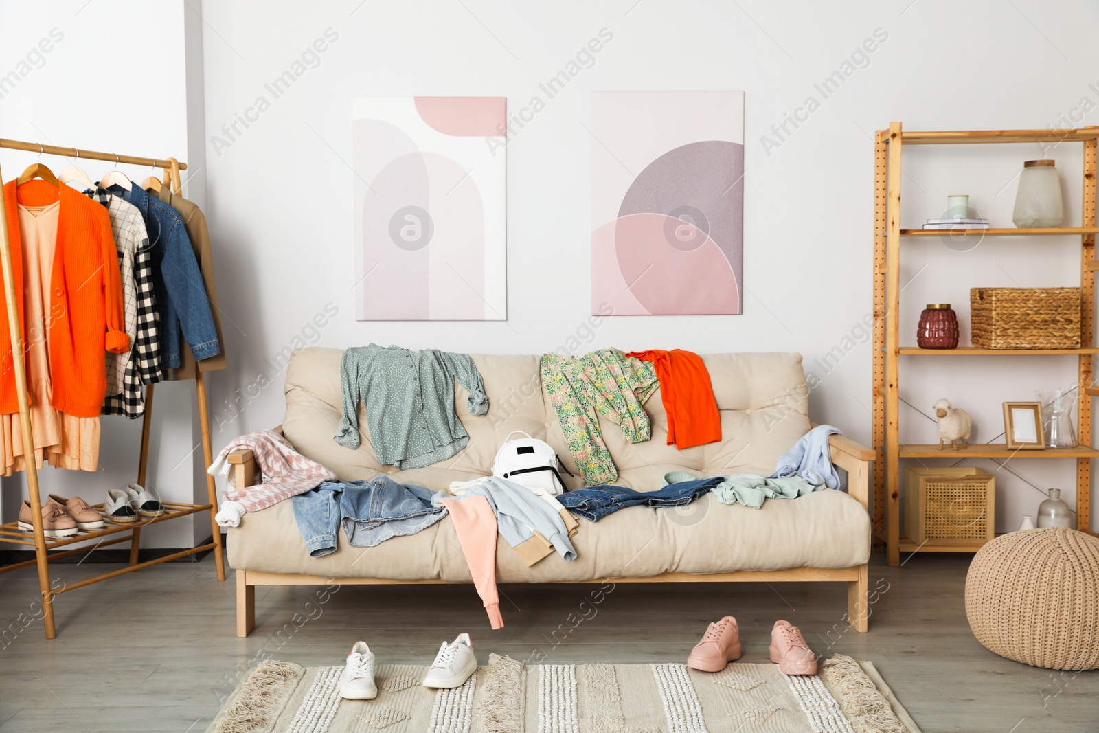 Photo of Messy pile of clothes on sofa and shoes in living room