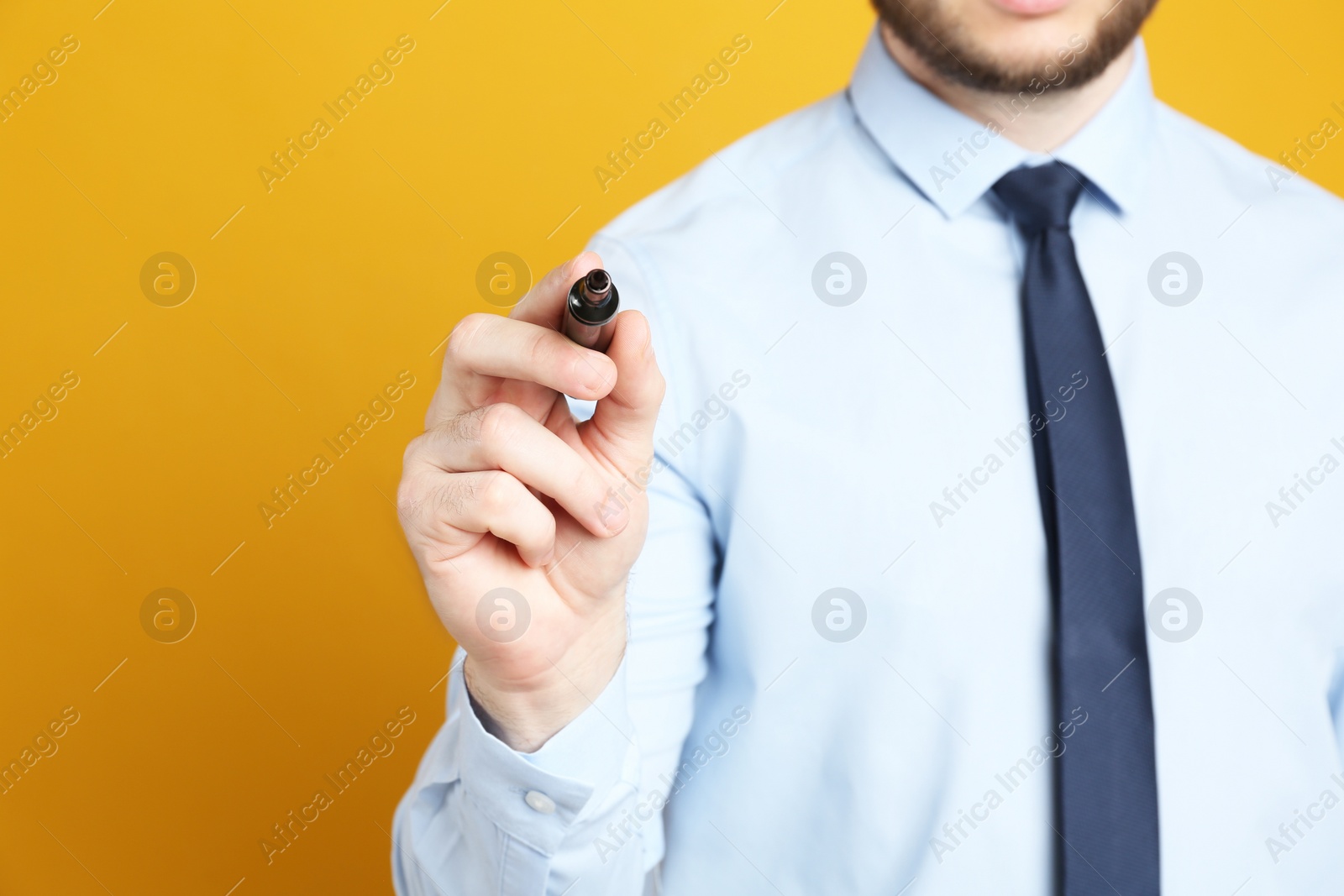 Photo of Businessman with marker against orange background, focus on hand