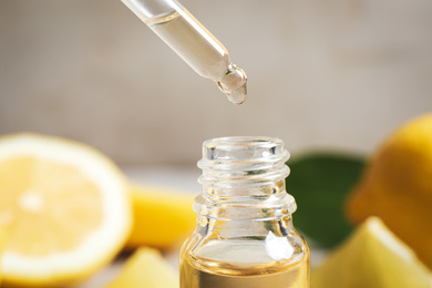 Photo of Citrus essential oil dripping from pipette into bottle, closeup