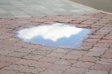 Photo of Reflection of sky in puddle on street tiles outdoors