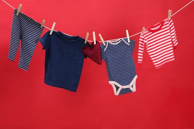 Different baby clothes and heart shaped cushion drying on laundry line against red background