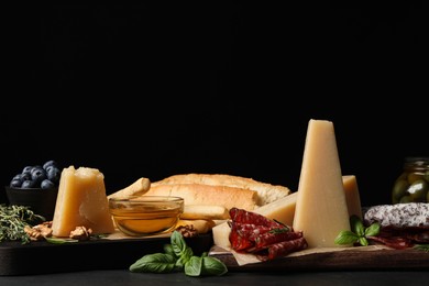 Photo of Delicious parmesan cheese, sausage slices, honey, bread and basil on grey table