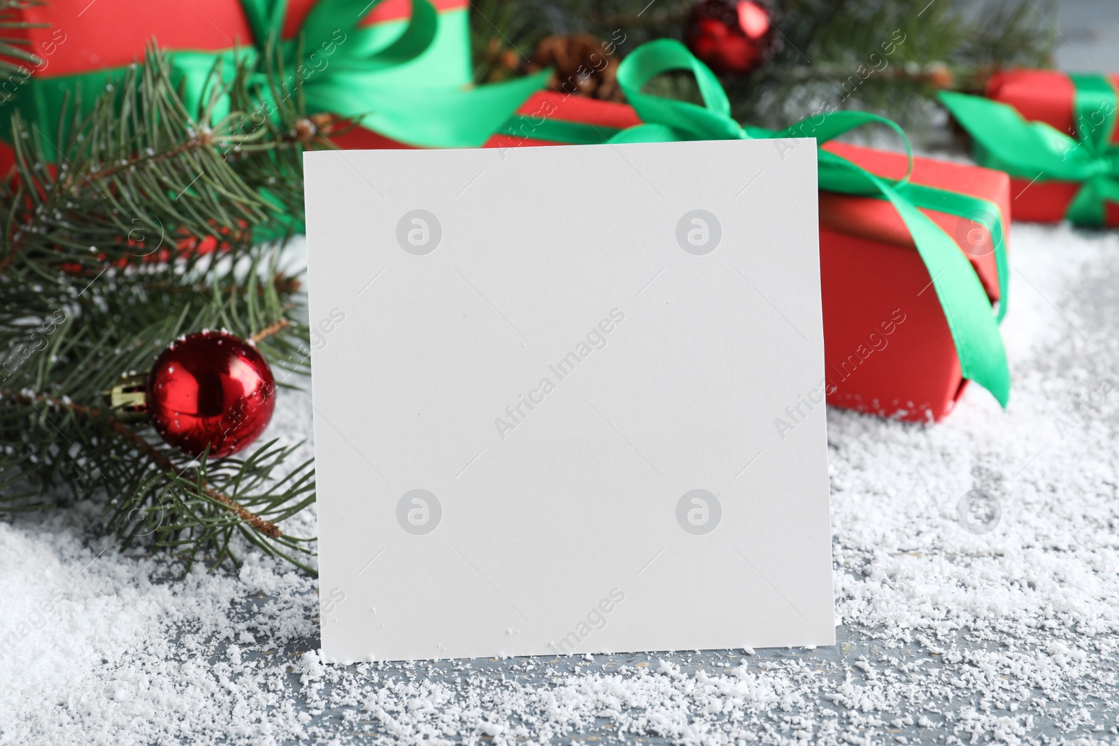 Photo of Blank greeting card near Christmas decorations on table with artificial snow, closeup. Space for text