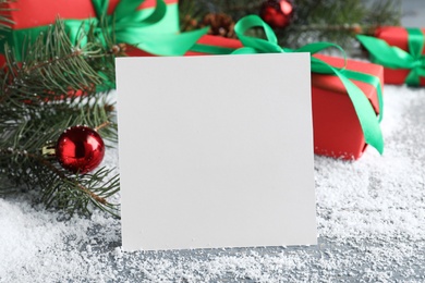 Photo of Blank greeting card near Christmas decorations on table with artificial snow, closeup. Space for text