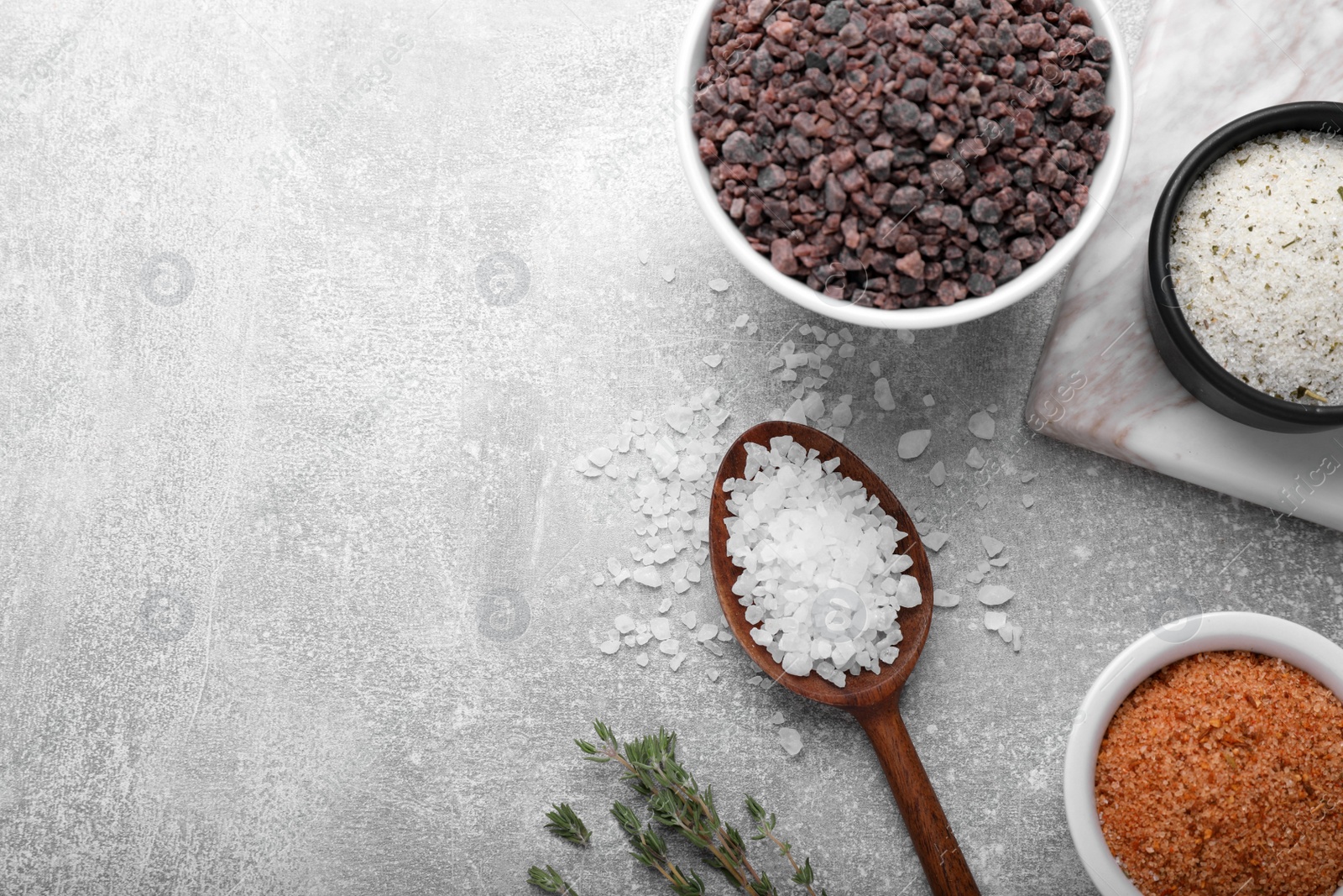 Photo of Different kinds of salt on grey table, flat lay. Space for text