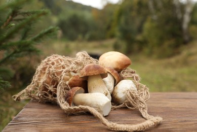 Photo of String bag and fresh wild mushrooms on wooden table outdoors