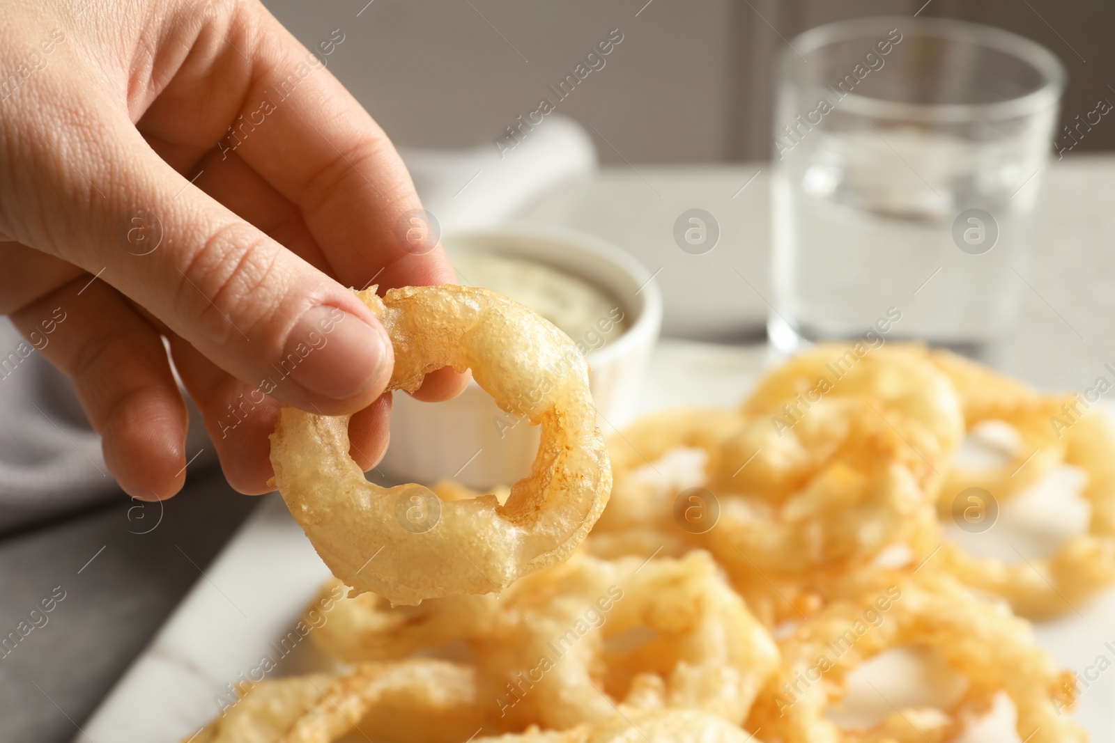 Photo of Woman holding homemade crispy onion ring over table, closeup