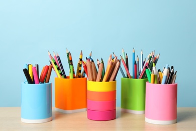 Photo of Holders with different school stationery on wooden table against light blue background. Back to school