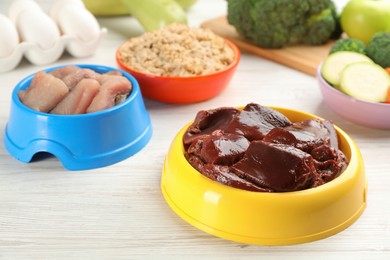 Natural pet food in feeding bowls on white wooden table, closeup